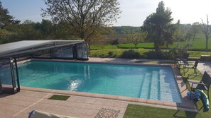 A swimming pool with a glass enclosure, surrounded by a patio with outdoor furniture and a view of a green landscape. - Cottage in the countryside with swimming pool (Saint-Colomb-De-Lauzun)