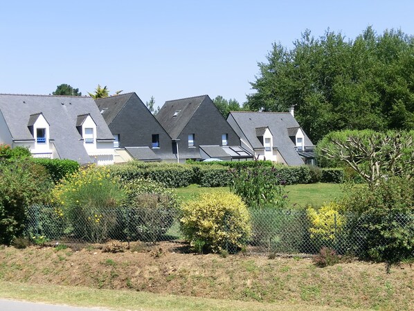 A row of modern houses with sloped roofs and small balconies, surrounded by well-maintained gardens and fences.