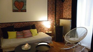 A cozy room with a brick wall, a white sofa with patterned cushions, a small table with a candle, and a white rocking chair. - Large apartment with view in 1900 villa (Plombières-les-Bains)