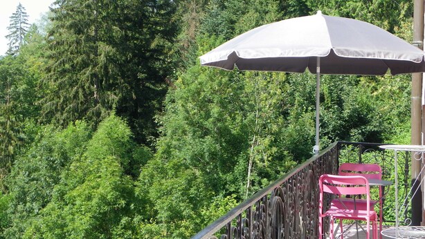 A balcony with a white umbrella, a metal railing, and two pink chairs. - Large apartment with view in 1900 villa (Plombières-les-Bains)
