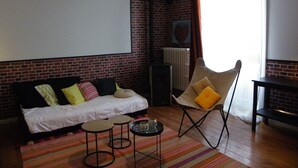 A cozy living room with a brick wall, a sofa with colorful cushions, a chair with a yellow cushion, and a small coffee table. - Large apartment with view in 1900 villa (Plombières-les-Bains)