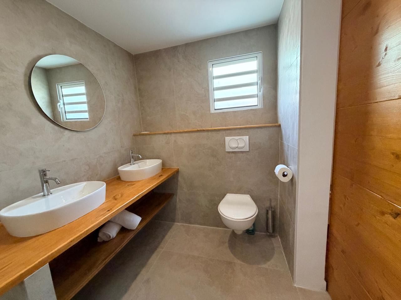 A bathroom with two sinks, a toilet, a mirror, and a window.
