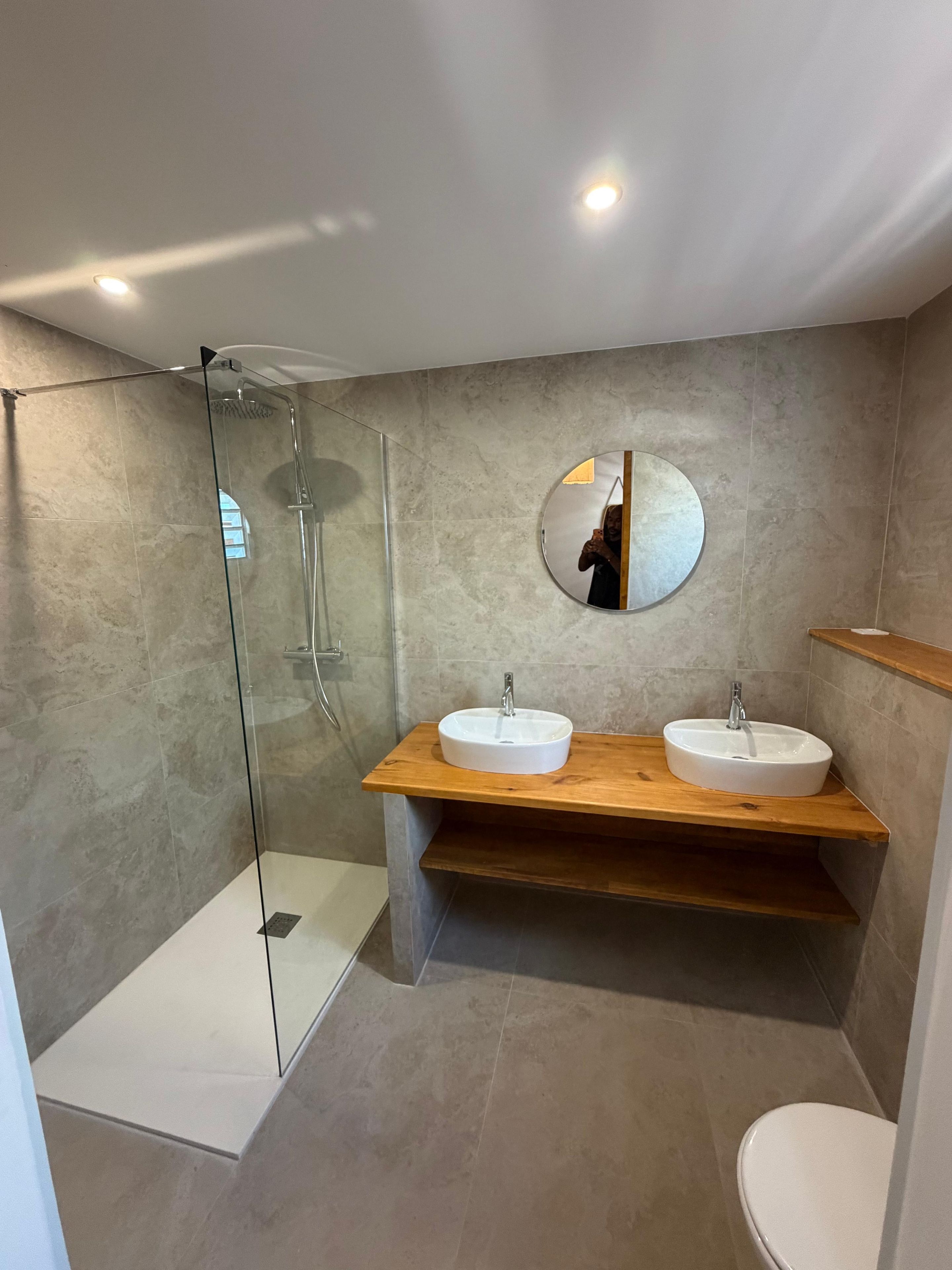 A modern bathroom with a glass-enclosed shower, two sinks, and a round mirror.