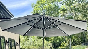 Eine Holzterrasse mit Tisch, Stühlen, einem Sonnenschirm und einem Grill.