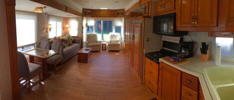 A compact RV interior with a kitchenette, dining area, and seating space.