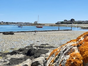 Cena costeira com barcos em águas calmas, um litoral rochoso e edifícios ao longe.