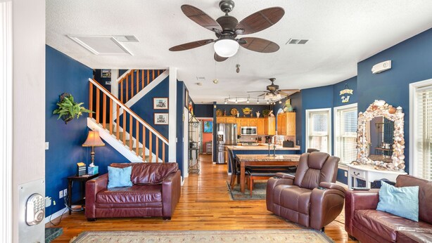 A spacious living room with a wooden floor, a ceiling fan, and a staircase leading to an upper level.