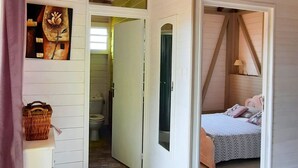 A room with a sloped ceiling, a bed, a bathroom, and a small table with a basket. - Pretty country bungalow (Saint-Esprit)