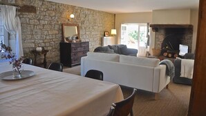 En hyggelig stue med en stenvæg, pejs, spiseplads med bord og en sofasætning.