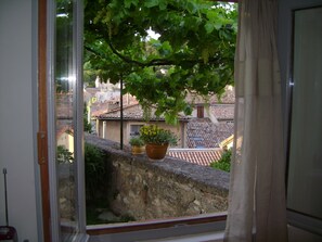 Ein Fenster mit Blick auf eine Steinmauer und einen Baum mit grünen Blättern.