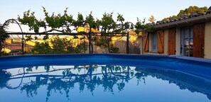 Ein Pool mit einer Pergola darüber, umgeben von einer Steinmauer und einem Gebäude mit Holzläden.