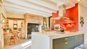 A modern kitchen with a large island, a brick fireplace, and a red accent wall. - Maison de Caractère with swimming pool Unbeatable view (Saint-Victurnien)