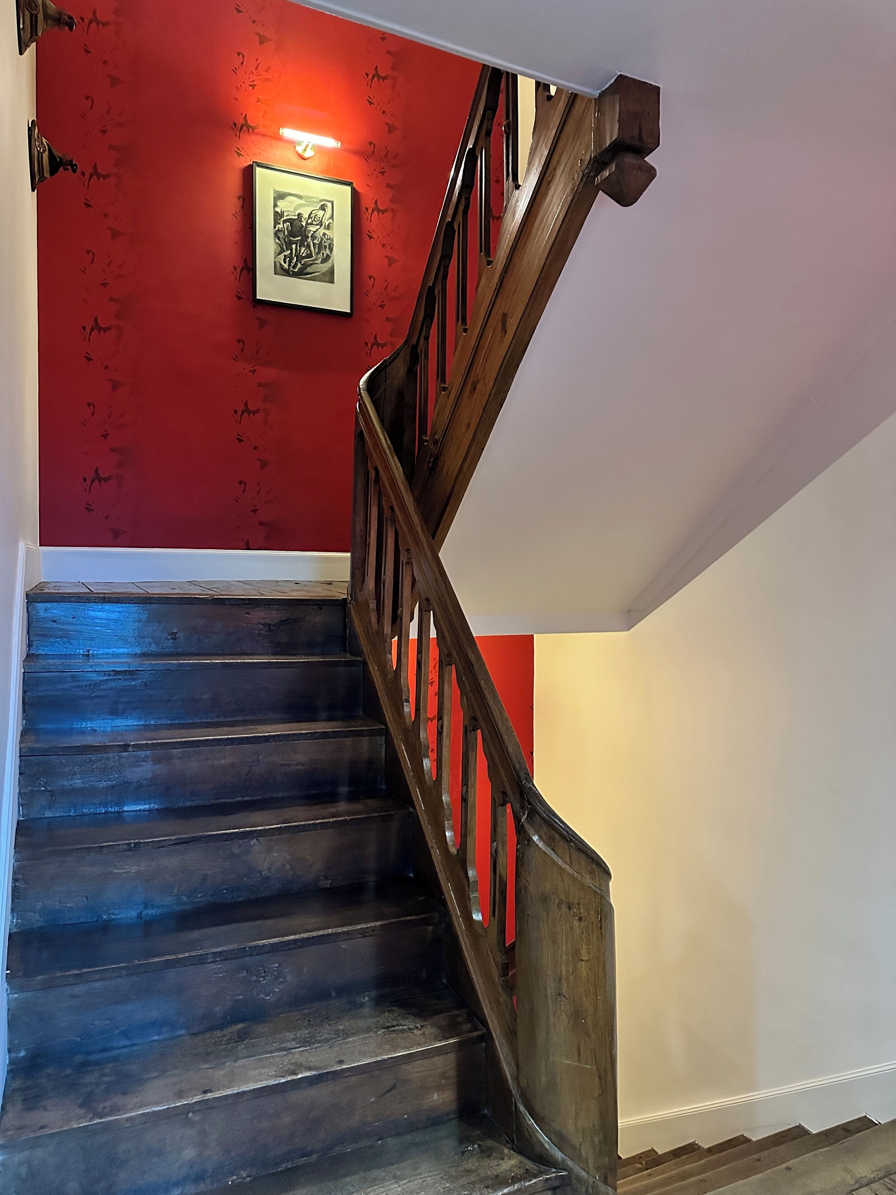 Una escalera de madera con una pared roja y un cuadro enmarcado.