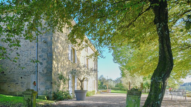 A building with a gravel driveway, a large tree, and a bench in the background. - Maison de Caractère with swimming pool Unbeatable view (Saint-Victurnien)