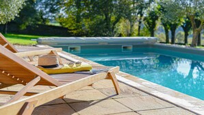 A poolside area with wooden lounge chairs, a hat, and sunglasses on one of the chairs. - Maison de Caractère with swimming pool Unbeatable view (Saint-Victurnien)