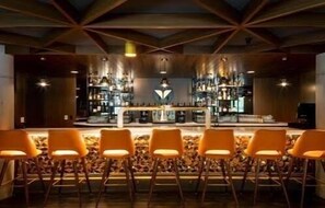 A bar area with a central bar counter, multiple bar stools, and a ceiling with a geometric pattern.