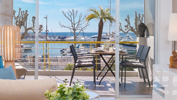 A balcony with a view of the marina, featuring a table with chairs, a potted plant, and a statue. - Want to GET AWAY from it all by the sea in GOLFE JUAN? (Vallauris)