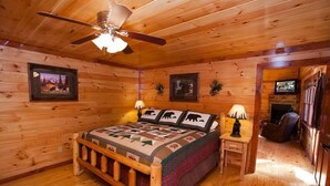 Ein Schlafzimmer in einer Blockhütte mit einem hölzernen Bett, einem Deckenventilator, zwei Wandleuchten und gerahmten Bildern.