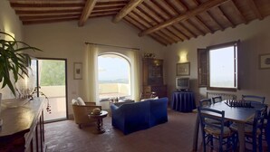 Un salón amplio con techo de madera, un ventanal grande, un sofá azul, una mesa de comedor con sillas y una televisión.
