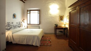Un dormitorio con cama, escritorio, silla, radiador, ventana y armario.