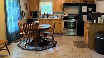 A kitchen with wooden cabinets, a dining table with chairs, a refrigerator, an oven, and a coffee maker.