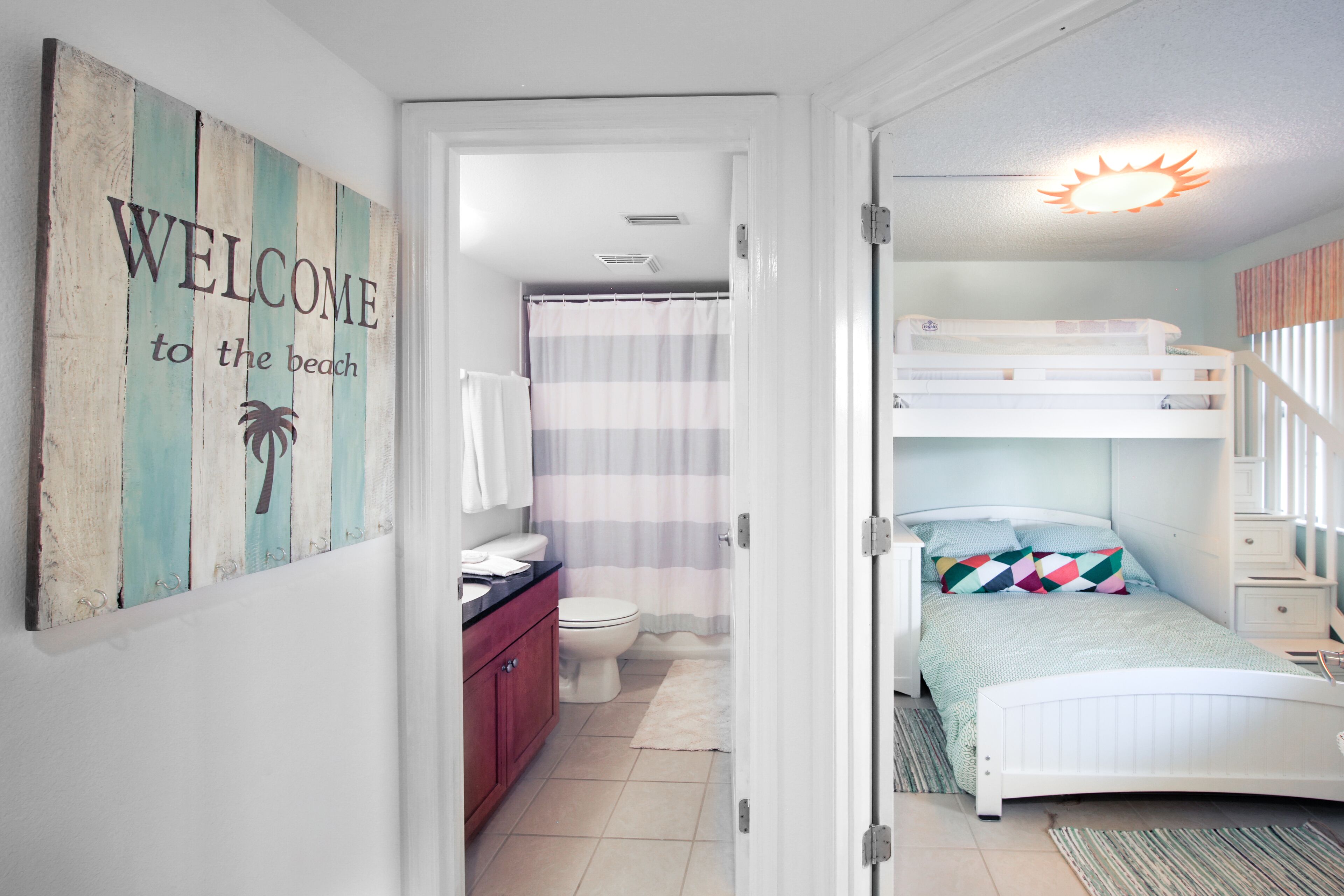 Une chambre avec un lit superposé, une salle de bain avec des toilettes et un rideau de douche, et un panneau d’accueil accroché au mur.