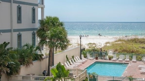A pool area with lounge chairs, a view of the beach, and a building with multiple windows.