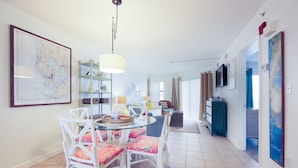 A dining area with a round glass table and white chairs, a hanging light fixture, and a map on the wall.