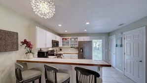 Una cocina moderna con armarios blancos, una isla de madera con taburetes de bar y una lámpara de techo decorativa.