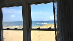 A view through a window of a beach with sand and ocean. - SEA GLASS OCEANFRONT COTTAGE.  (Nags Head)