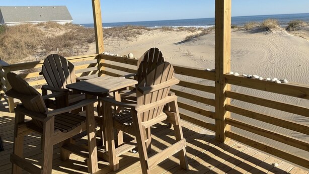 A wooden deck with Adirondack chairs overlooking a sandy beach and ocean. - SEA GLASS OCEANFRONT COTTAGE.  (Nags Head)