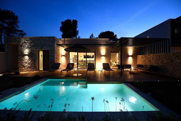 A modern house with a swimming pool, outdoor seating, and stone walls.