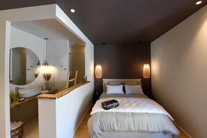 A modern hotel room with a large bed, a built-in vanity with a mirror, bedside lamps, and a suitcase on the bed.