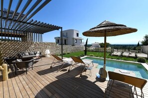 A wooden deck with lounge chairs, a pool, and a pergola.