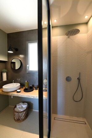 A modern bathroom with a round mirror, a sink, a shower, and a small window.