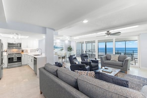 A modern living space with a kitchen, dining area, and a balcony with a view of the ocean. - Beach, Sand, Sun! (Indian Rocks Beach)