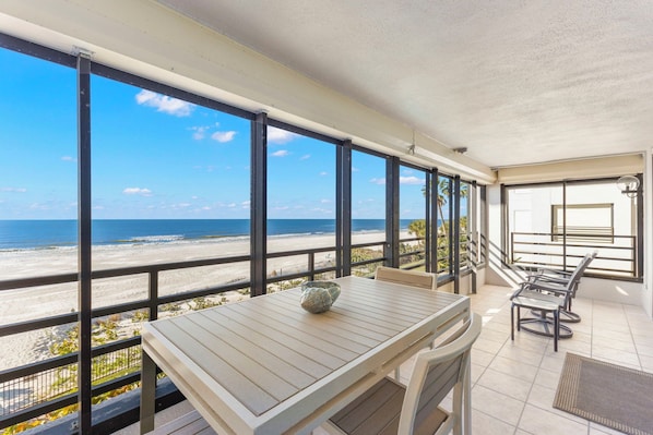 A balcony with a view of the beach, a table with chairs, and a small decorative bowl. - Beach, Sand, Sun! (Indian Rocks Beach)