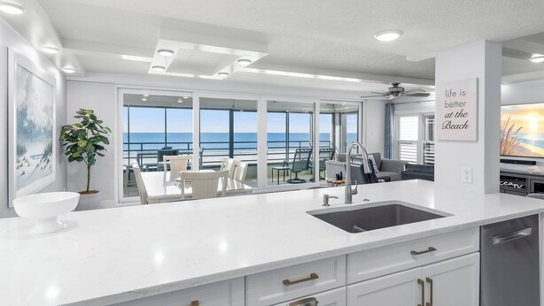 Una cocina moderna con una isla grande, muebles blancos y vista al océano.