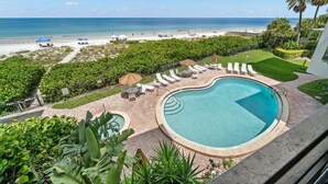Piscina con sillas de descanso y sombrillas, rodeada de vegetación, con vista a la playa y al océano.