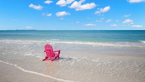 Una playa con una sola silla rosa mirando al océano.