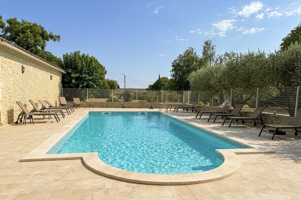 Una piscina rectangular con una solana empavedada, rodeada de sillas de descanso y un muro de piedra.
