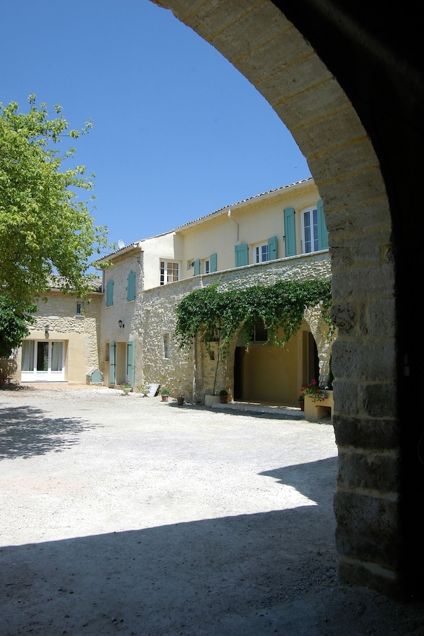 Un patio con un arco de piedra, un edificio de fachada amarilla y un árbol.