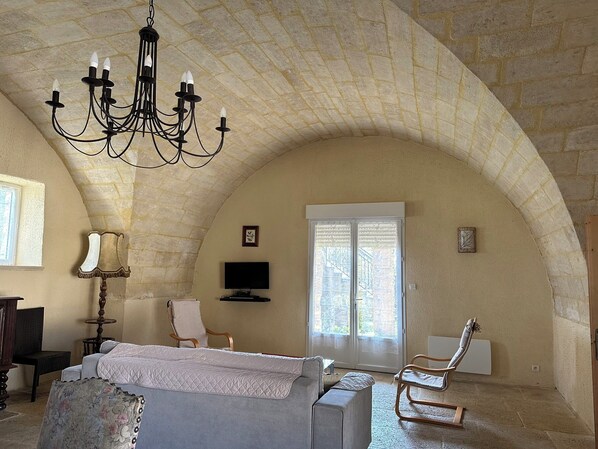 A room with a high arched ceiling, a chandelier, a bed, a television, and a window with blinds.