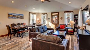 A spacious living room with a dining area, leather furniture, a ceiling fan, and a bookshelf.