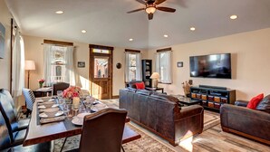 A spacious living room with a dining area, a ceiling fan, and a flat-screen TV.
