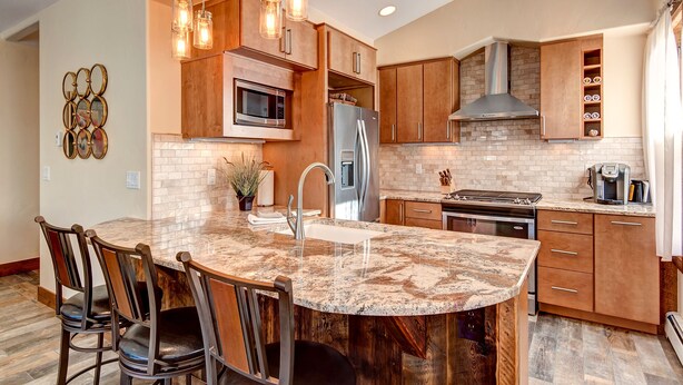 A modern kitchen with a central island, stainless steel appliances, wooden cabinetry, and pendant lighting.