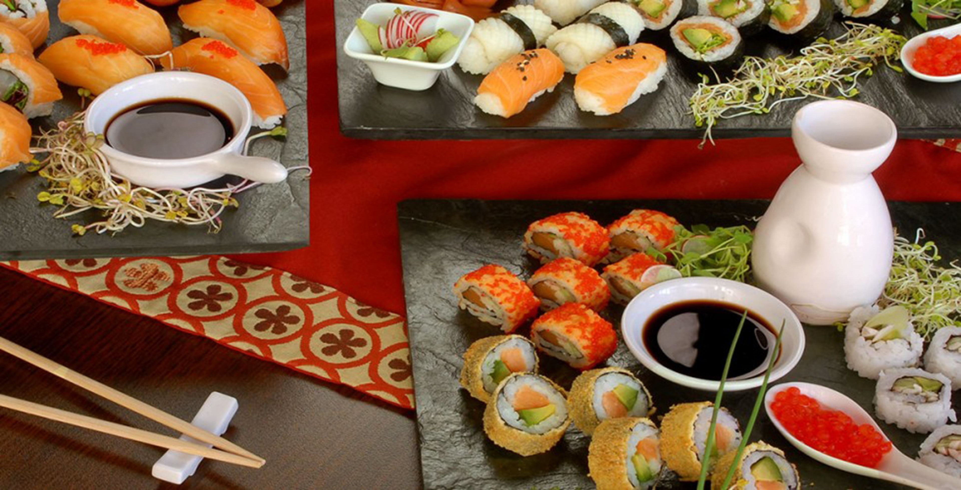 A variety of sushi dishes on a table with chopsticks and a small bowl of soy sauce.