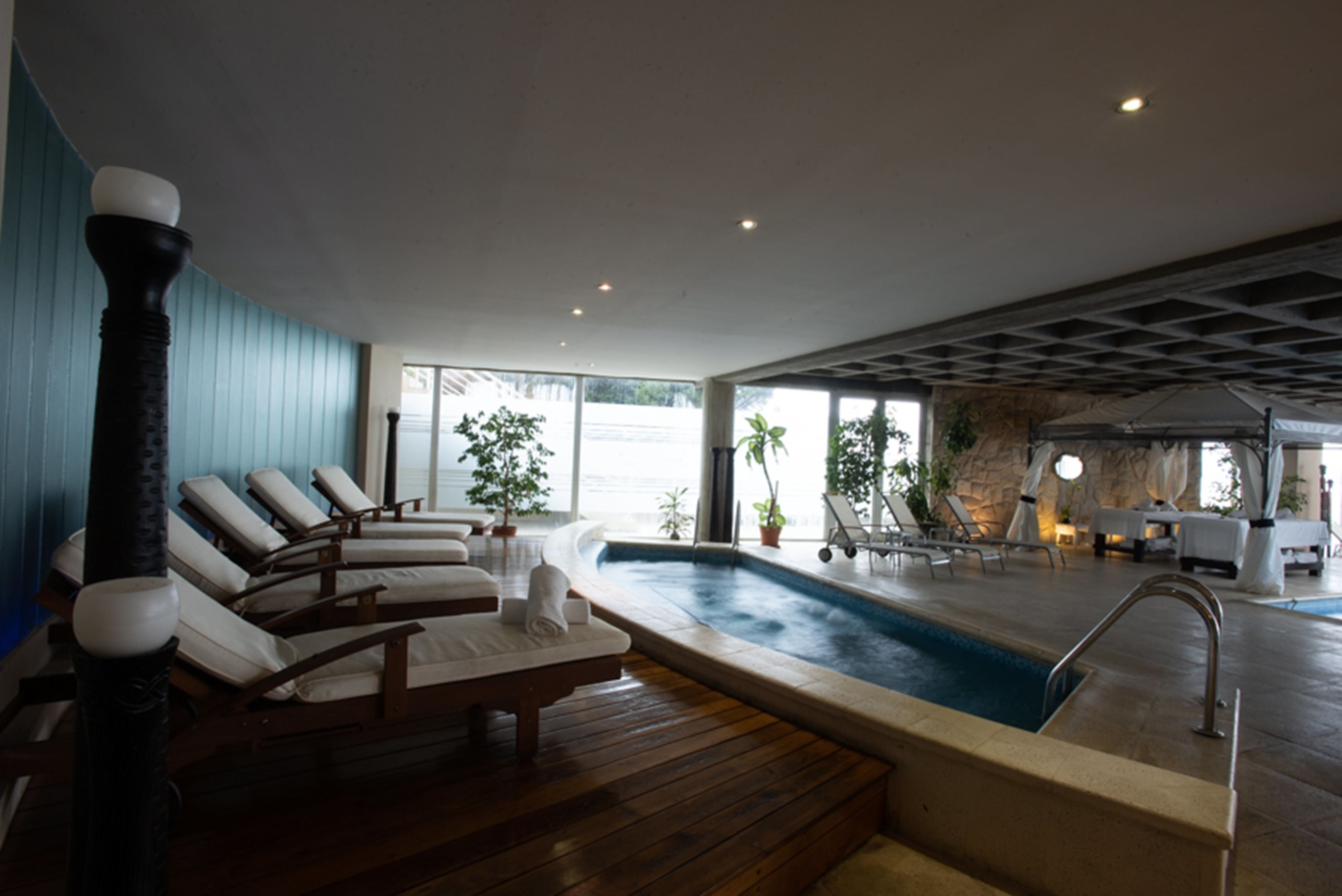 A modern indoor pool area with lounge chairs, a small pool, and a stone wall.