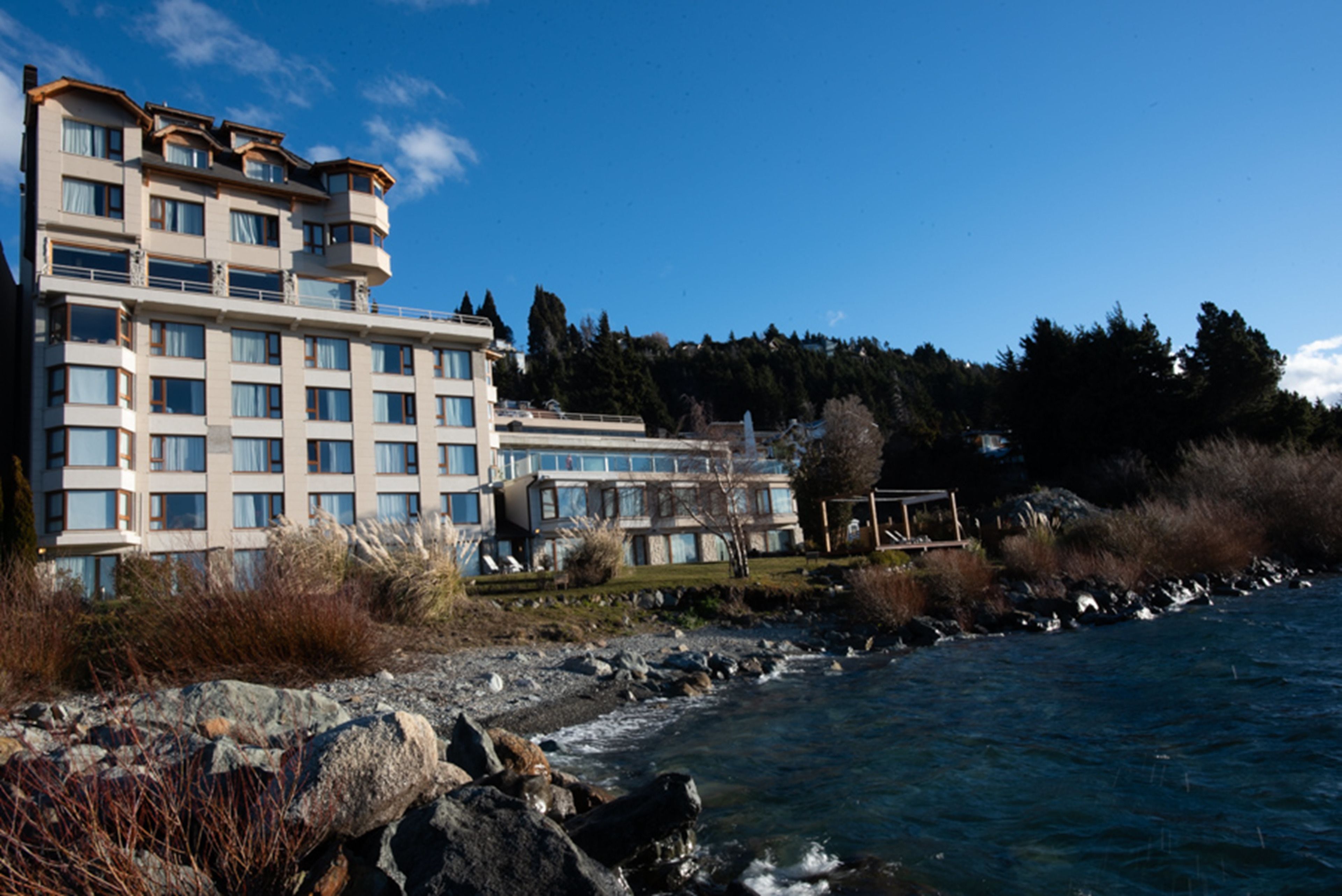 Un hôtel à plusieurs étages, doté d’une architecture moderne, situé au bord d’une côte rocheuse et offrant une vue sur l’eau.