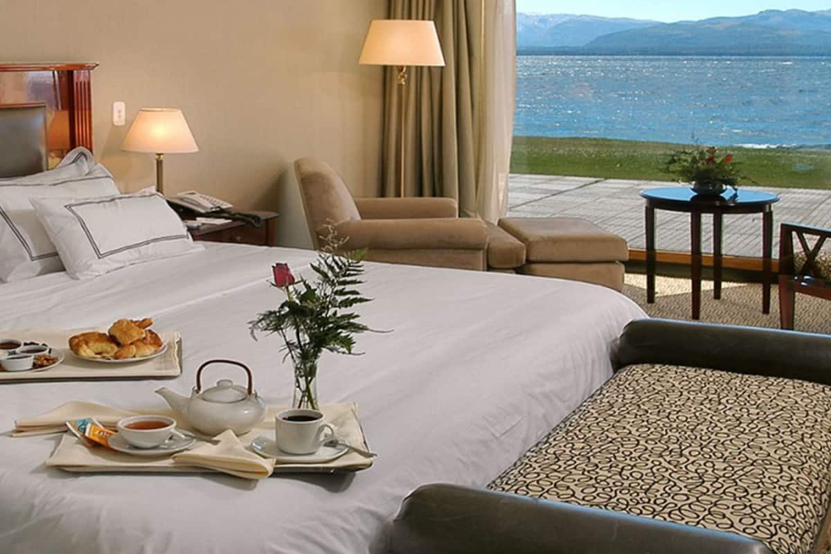 A hotel room with a bed, breakfast tray, tea set, and a view of the sea.